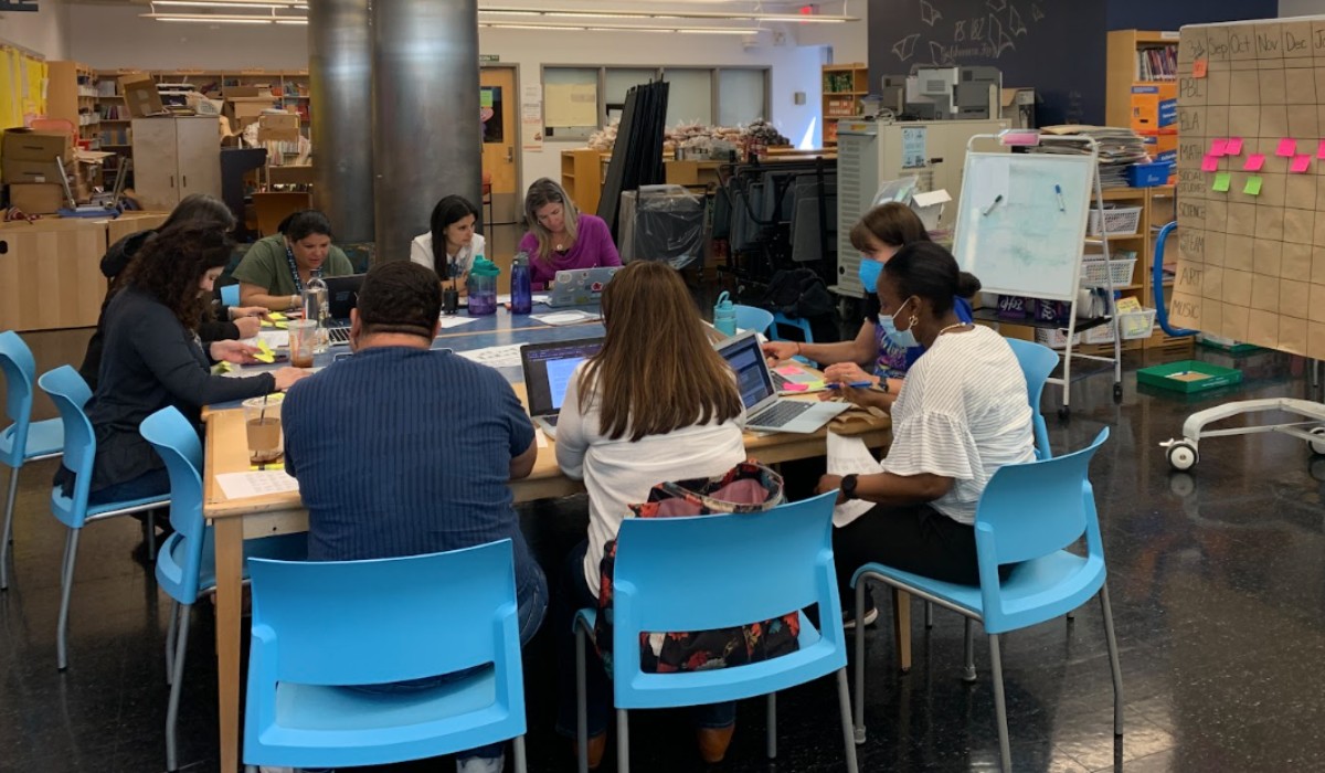 Adults sitting around a square table in a classroom working on laptops